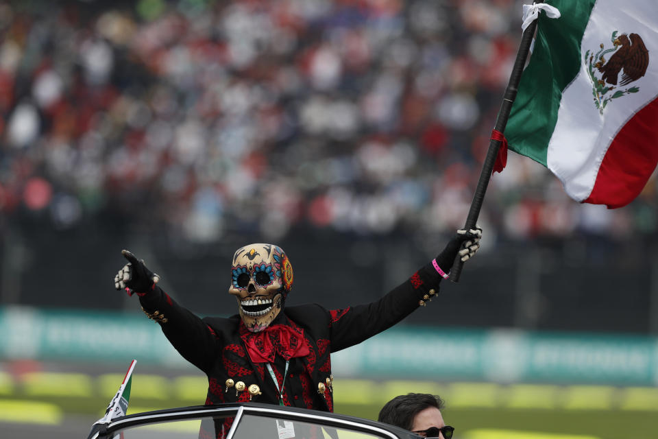 In this Oct. 27, 2019 photo, a man dressed as a Day of the Dead skeleton holds a Mexican flag as he rides the lead car during the opening parade of the Formula One Mexico Grand Prix auto race at the Hermanos Rodriguez racetrack in Mexico City. (AP Photo/Rebecca Blackwell)