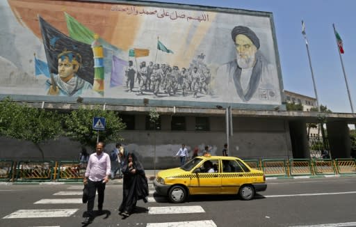 Iranians walk under a mural of Ayatollah Ruhollah Khomeini, who remains a guiding figure in the country 30 years after his death