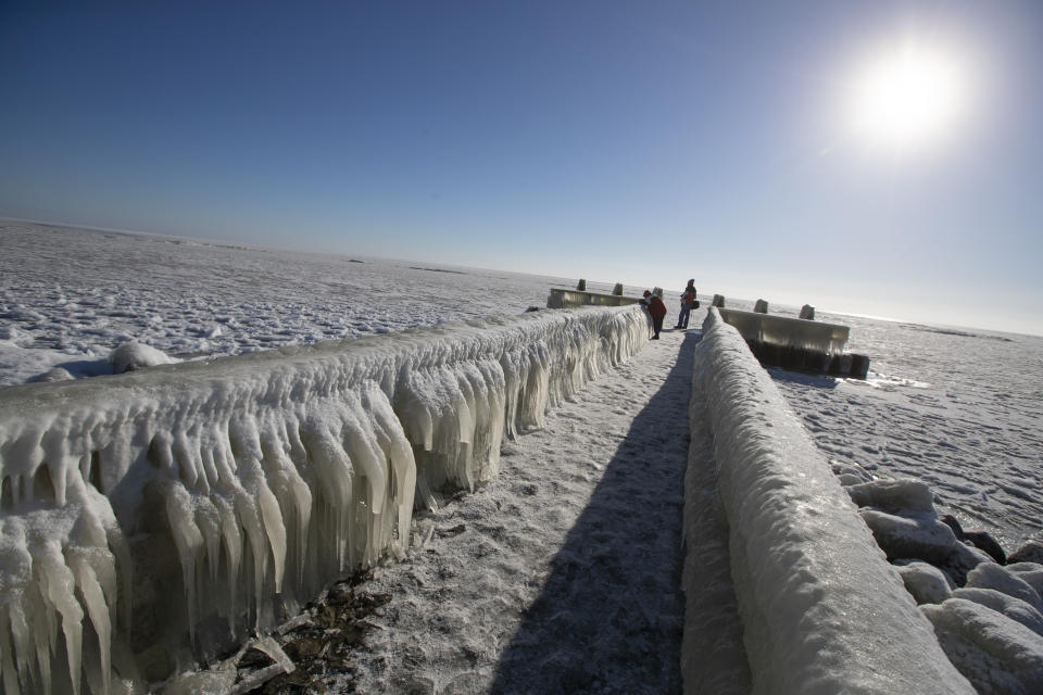 People take pictures of icicles on a jetty at the Afsluitdijk, a dike separating IJsselmeer inland sea, rear, and the Wadden Sea, Netherlands, Thursday, Feb. 11, 2021. The deep freeze gripping parts of Europe served up fun and frustration with heavy snow cutting power to some 37,000 homes in central Slovakia. (AP Photo/Peter Dejong)