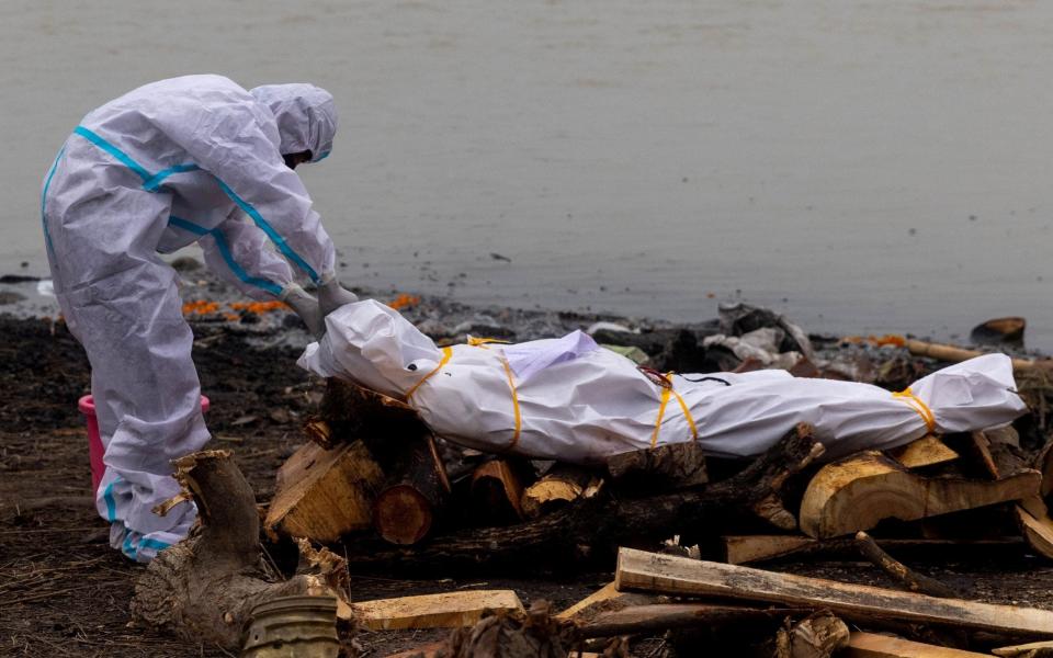 A man wearing a protective suit touches the body of his relative, who died from Covid-19 before his cremation on the banks of the river Ganges at Garhmukteshwar - DANISH SIDDIQUI / REUTERS 