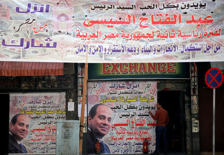 A man is seen in front of an exchange bureau, with an advertisement showing images of the U.S. dollar and other foreign currency and a poster supporting Egypt's President Abdel Fattah al-Sisi for the upcoming presidential election in Cairo, Egypt March 14, 2018. REUTERS/Amr Abdallah Dalsh?