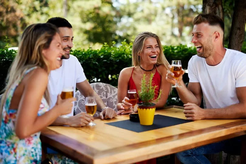 Happy friends sitting at a table in a summer bar laughing and drinking beer