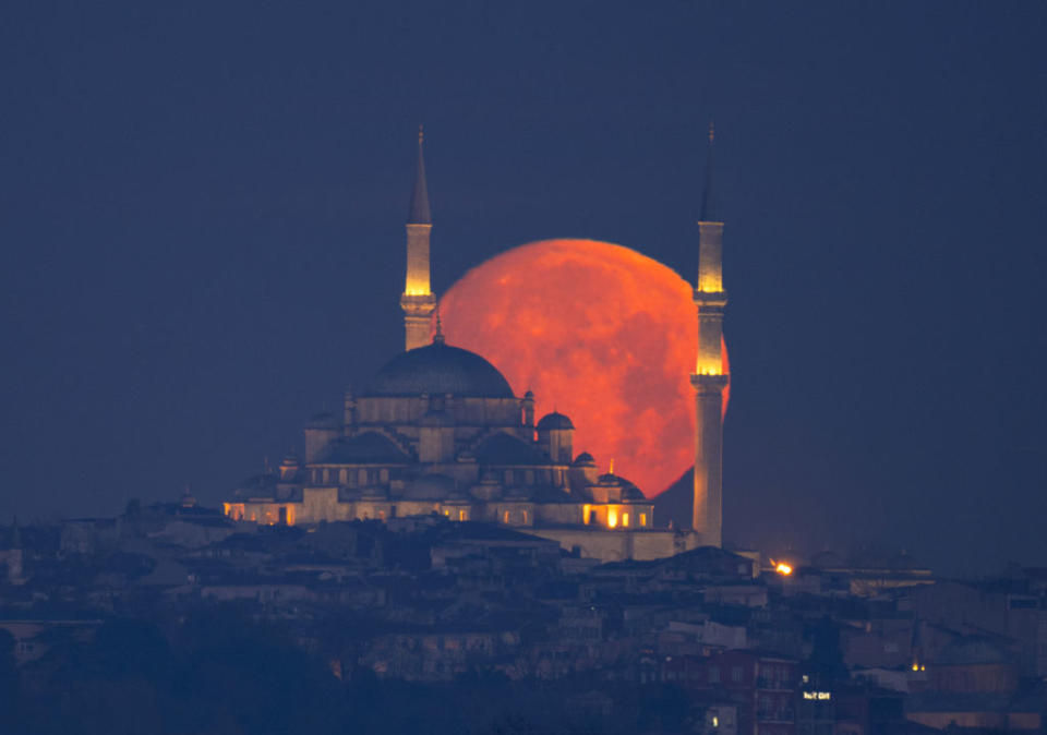 The full moon appears red as it rises from behind a temple