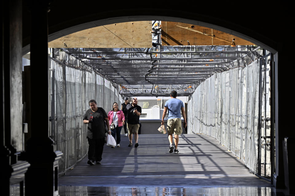 People walk across a pedestrian bridge that will be shrouded with window screens and fencing to prevent viewing of the upcoming race. 