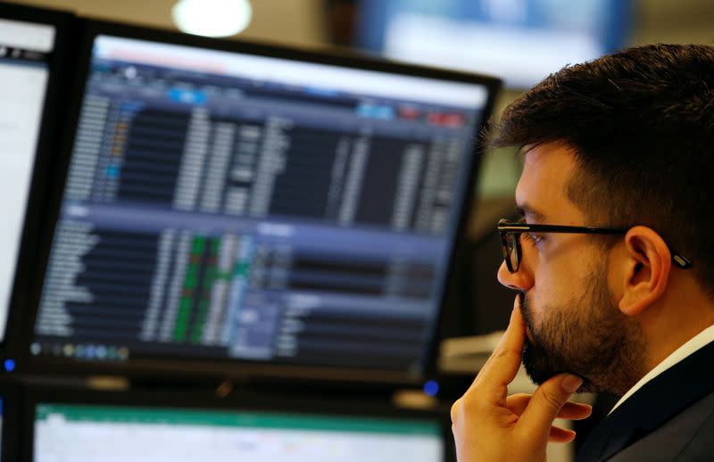 Trader works at his desk whilst screens show market data at CMC Markets in London