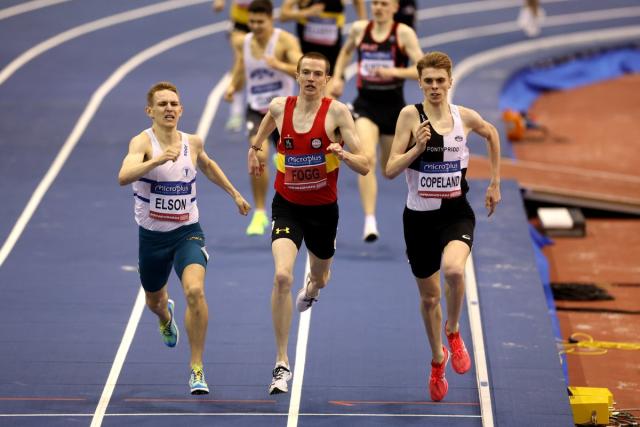 Female athlete taking position on her marks to start off the run. Side view  of female runner sitting at the start line on running track on a black  background. stock photo