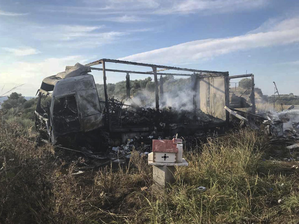 A burnt out truck on a field behind a small chapel, next to a motorway, following a collision near Greece's northern town of Kavala, Saturday, Oct. 13, 2018. A car carrying migrants collided with a truck in northern Greece on Saturday, killing 11 people, police said. (Proininews.gr via AP)