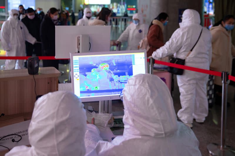 Workers in protective suits monitor a screen showing the thermal scan to check temperatures of passengers arriving at the Nanjing Railway Station, following the outbreak of a new coronavirus, in Nanjing