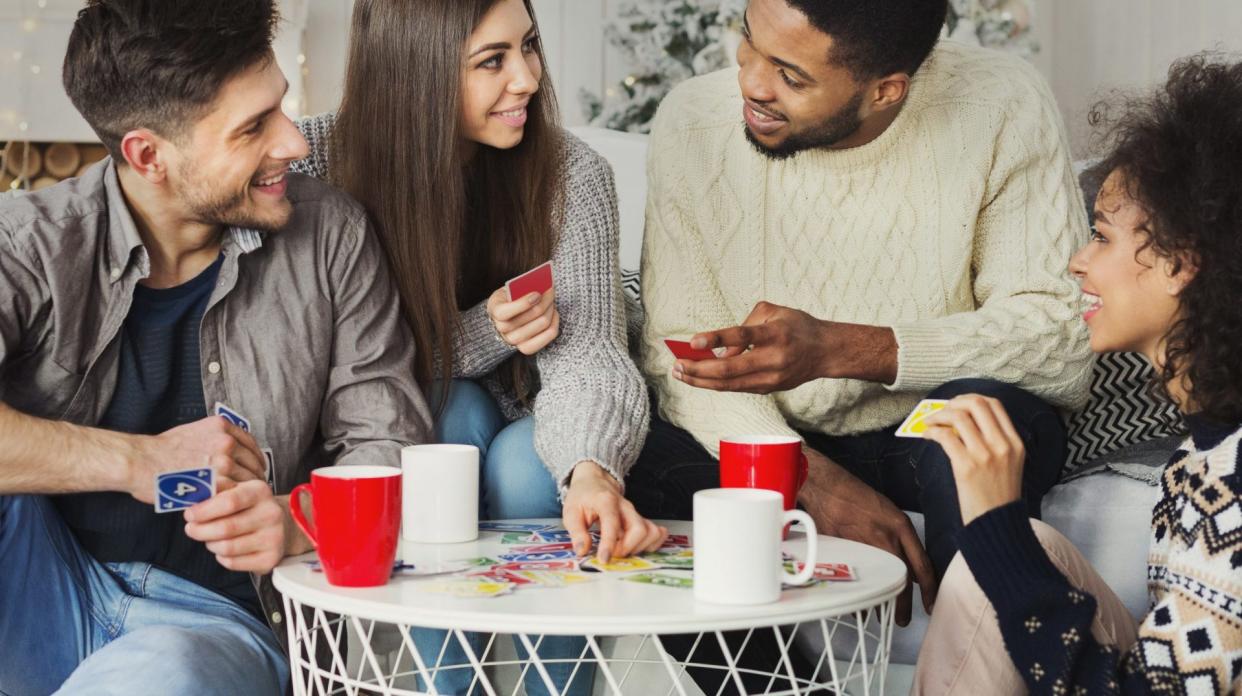 Multiracial friends having fun and playing game of cards UNO against christmas tree.