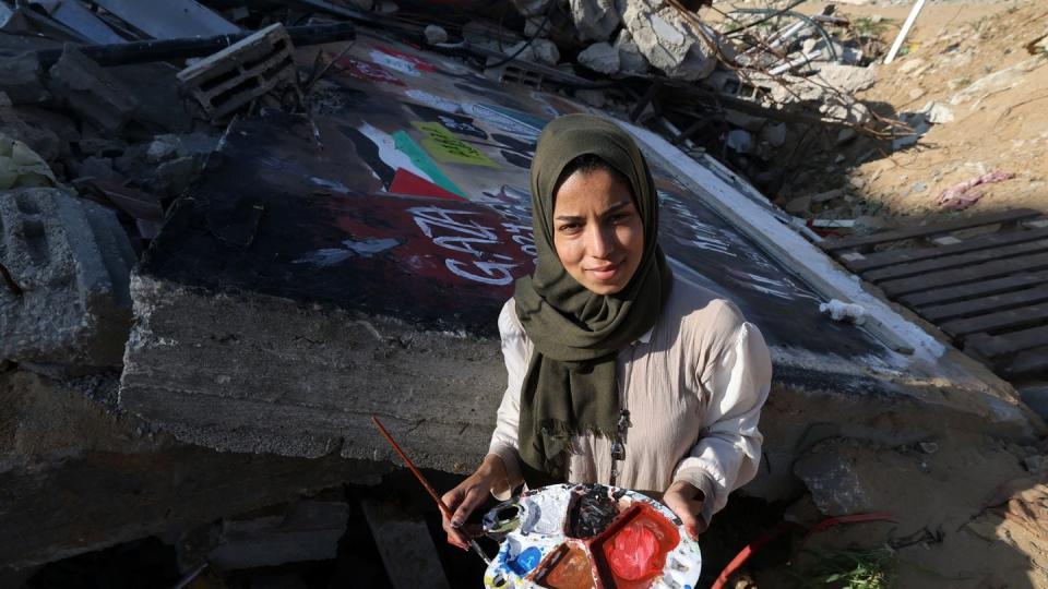 Displaced Palestinian artist Amal Abo stands next to her painting on the wall of a house destroyed during Israeli bombing in Rafah in the Gaza Strip on Dec. 31, 2023. (AFP via Getty Images)