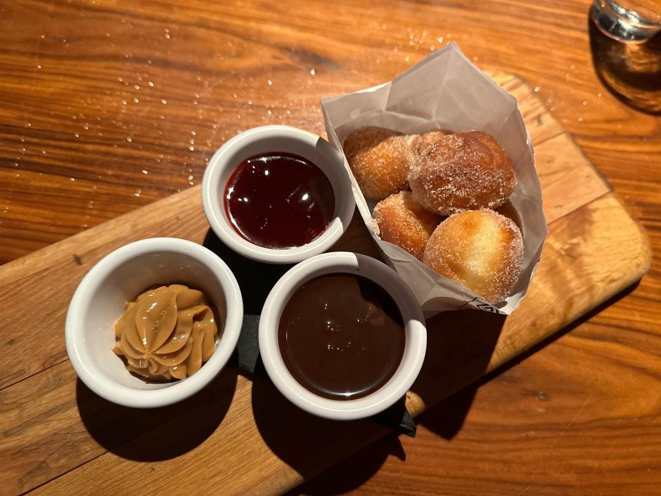 A packet of golden-brown doughnuts with three different sauces on the side. The sauces are chocolate, caramel, and berry flavors