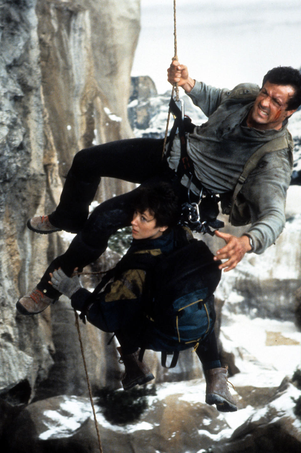 Sylvester Stallone and Janine Turner hanging by ropes off the side of a cliff in a scene from the film 'Cliffhanger', 1993. (Photo by Carolco Pictures/Getty Images)