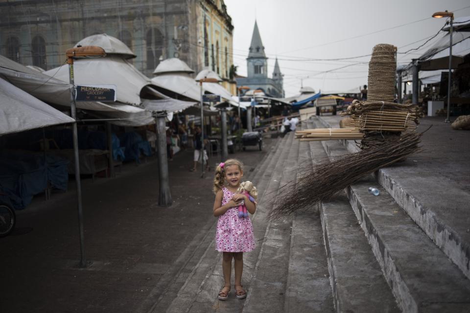 In this Aug. 31, 2019 photo, Valeria, 6, poses for a picture embracing her doll inside the Ver-o-Peso riverside market in Belém, Brazil. The stands at the Ver-O-Peso sell maracas with feathers made by the indigenous peoples of the Amazon, ceramics and handcrafts made with coconut shells. (AP Photo/Rodrigo Abd)