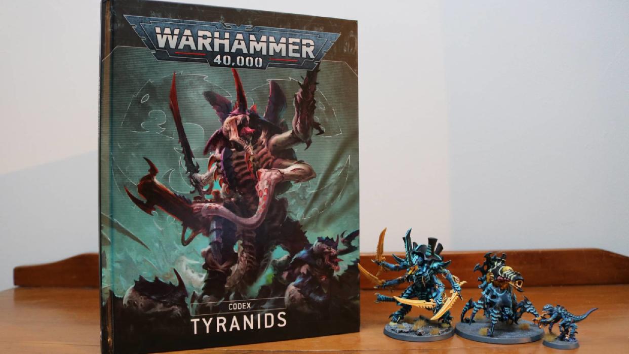  The Tyranid Codex on a wooden table, beside some miniatures. 