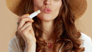 Beach vacation. Closeup on woman isolated on beige with summer hat and hygienic lipstick.