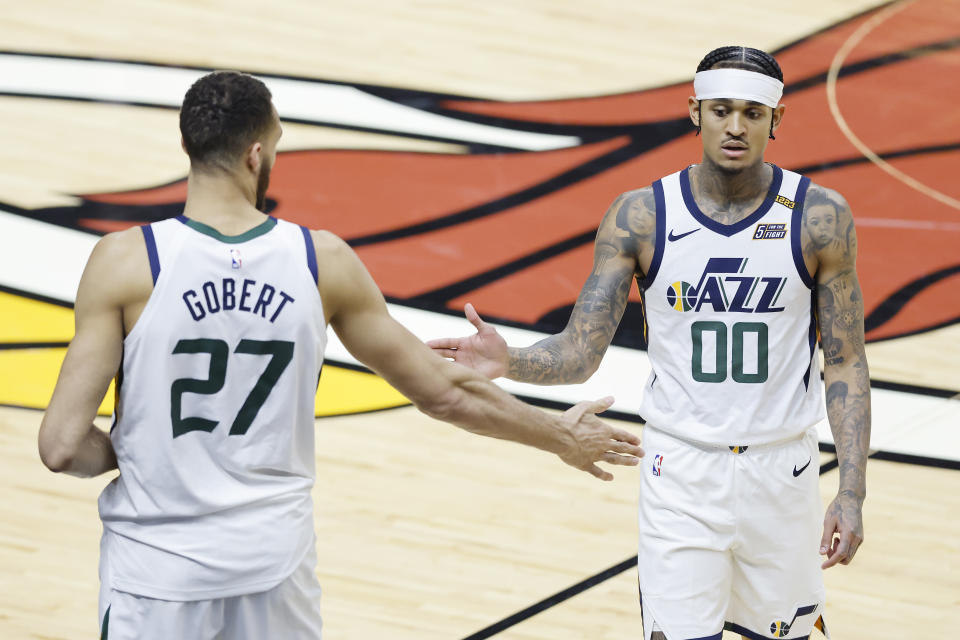 Rudy Gobert, facing away from the camera, extends his hand to slap Jordan Clarkson's hand on the court during a game.