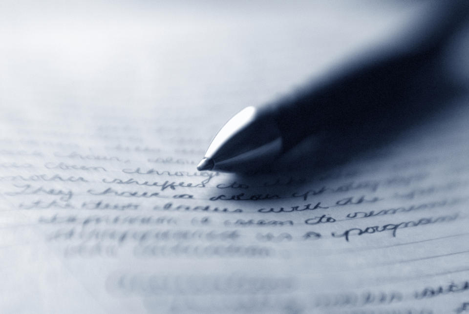 A close-up image of a pen writing on a piece of paper filled with handwritten text. The text is blurred and not legible