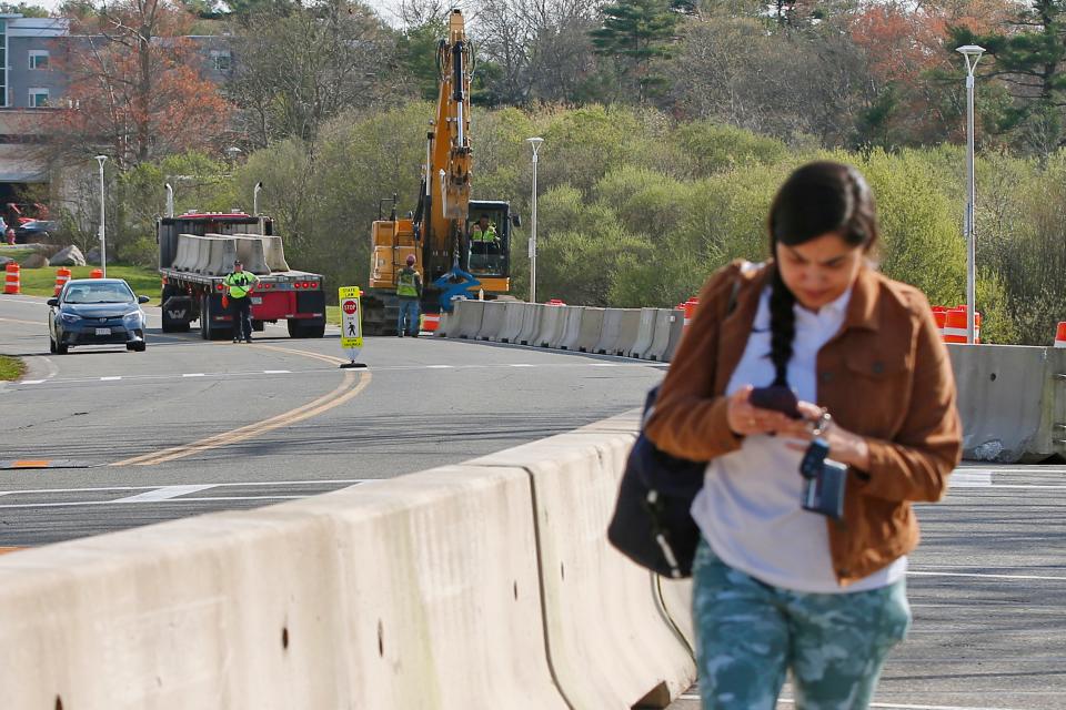 A student walks on the edge of Ring Road at UMass Dartmouth as crews install concrete barriers for protection, two weeks after a student was killed by a motorist.