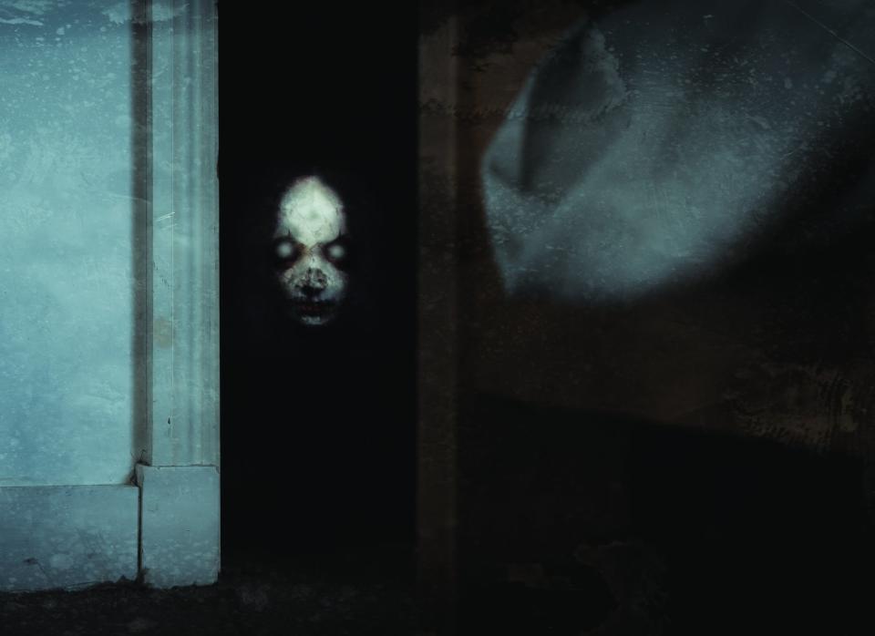 Spooky image with a skull-like face peering from the darkness beside a frosted window