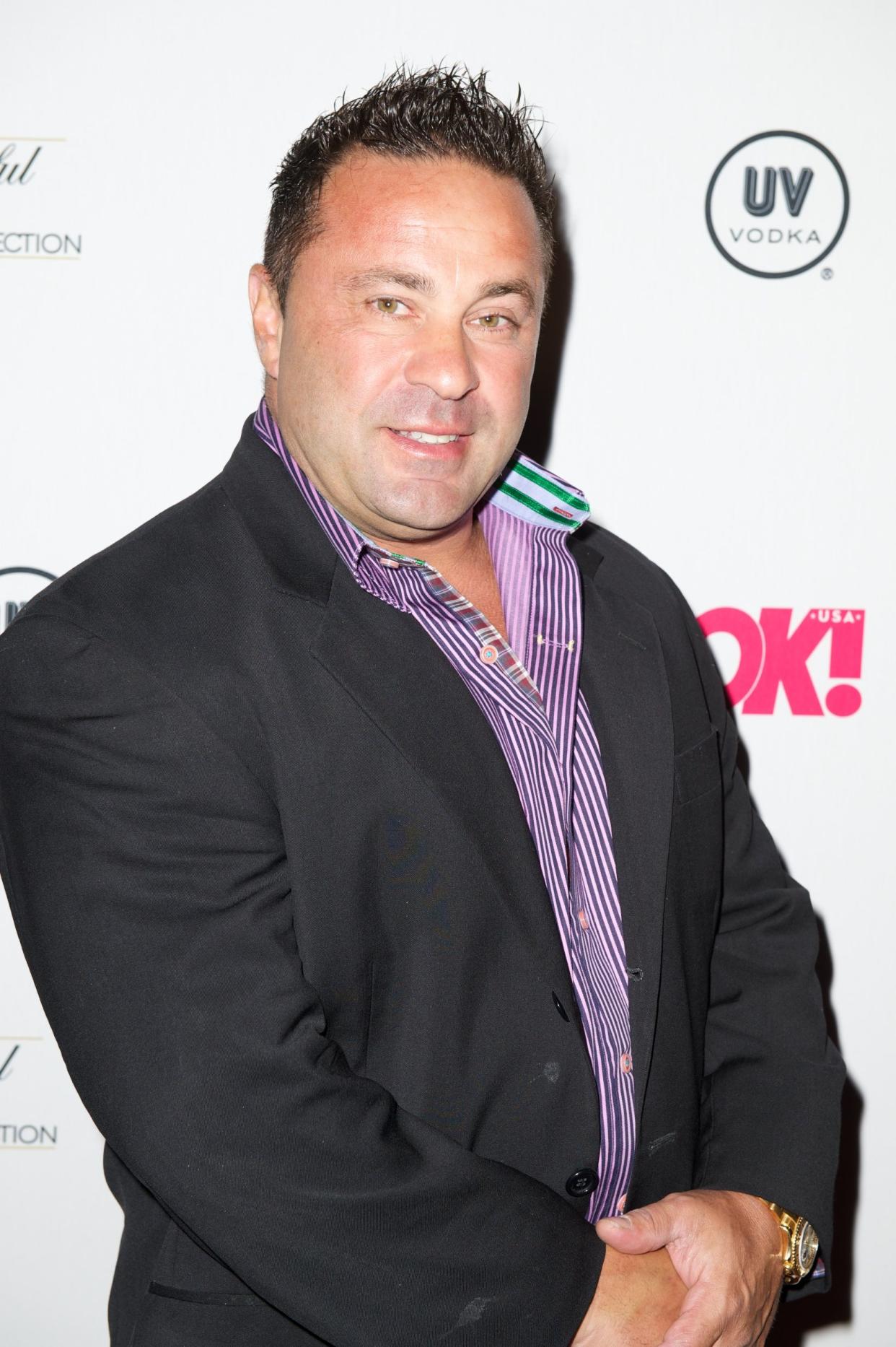 Joe Giudice poses wearing a suit jacket and purple and white striped shirt