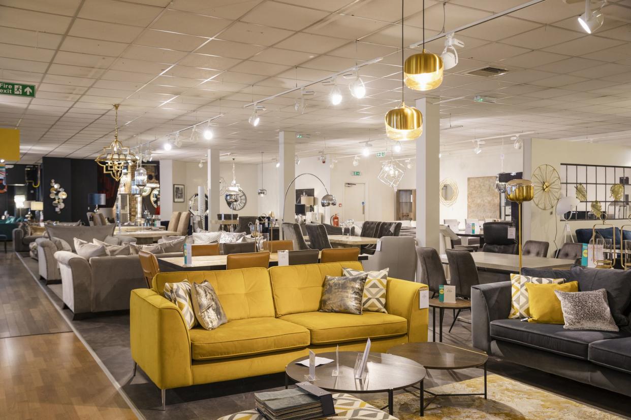 A wide angle of a furniture store with no people in. There is various different sofas and lamps and furniture on the shop floor for display purposes.