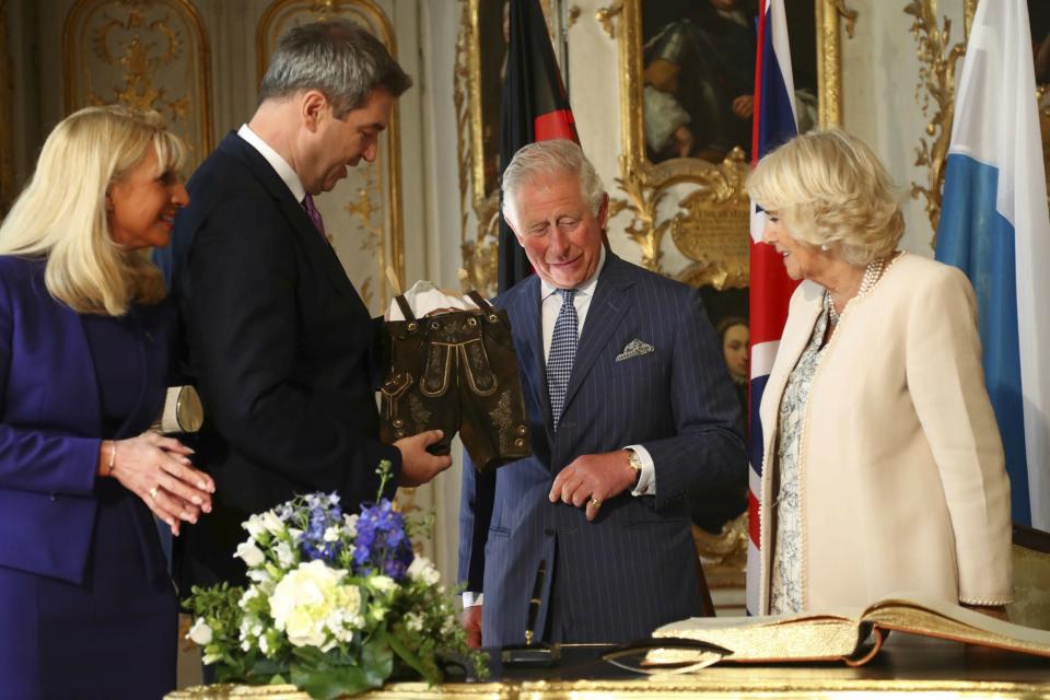 Bavarian State Premier Markus Soeder (2nd L) and his wife Karin Baumueller-Soeder (L) hand over traditional Bavarian leather trousers for the new born grandchild of Britain's Prince Charles, Prince of Wales (2nd R), and his wife Camilla (R), Duchess of Cornwall, after signing the guest book in Munich, southern Germany, on May 9, 2019. (Photo by Matthias Schrader / POOL / AFP)        (Photo credit should read MATTHIAS SCHRADER/AFP via Getty Images)