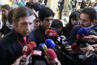 Eagles of Death Metal singer Jesse Hughes, left, and guitarist Eden Galindo, center, answer reporters outside the special court room, Tuesday, May 17, 2022 in Paris. Performers from rock band Eagles of Death Metal are appearing in a Paris court to testify about the night Islamic State extremists stormed their concert at the Bataclan theater, killing scores of people in France's worst terrorist attack in generations. The band members, singer Jesse Hughes and guitarist Eden Galindo, are among the survivors and witnesses to the Nov. 13, 2015 attacks, and are civil parties to the case. (AP Photo/Christophe Ena)
