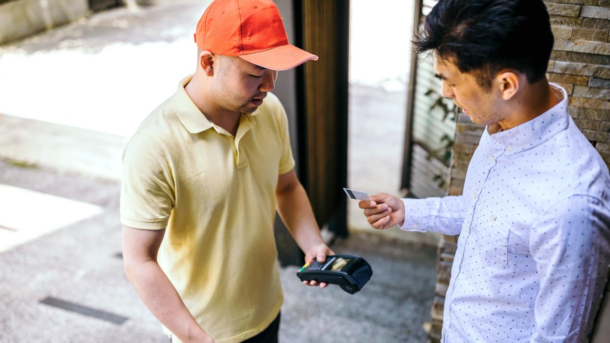 Photo of asian man paying for his food delivery at home with credit card.