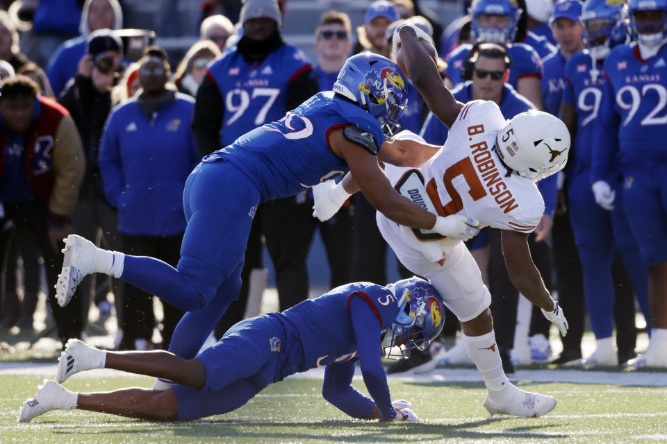 Texas running back Bijan Robinson (5) rushes for a first down as Kansas defensive lineman Malcolm Lee (99) and safety O.J. Burroughs (5) make the stop during the first quarter of an NCAA college football game on Saturday, Nov. 19, 2022, in Lawrence, Kan. (AP Photo/Colin E. Braley)