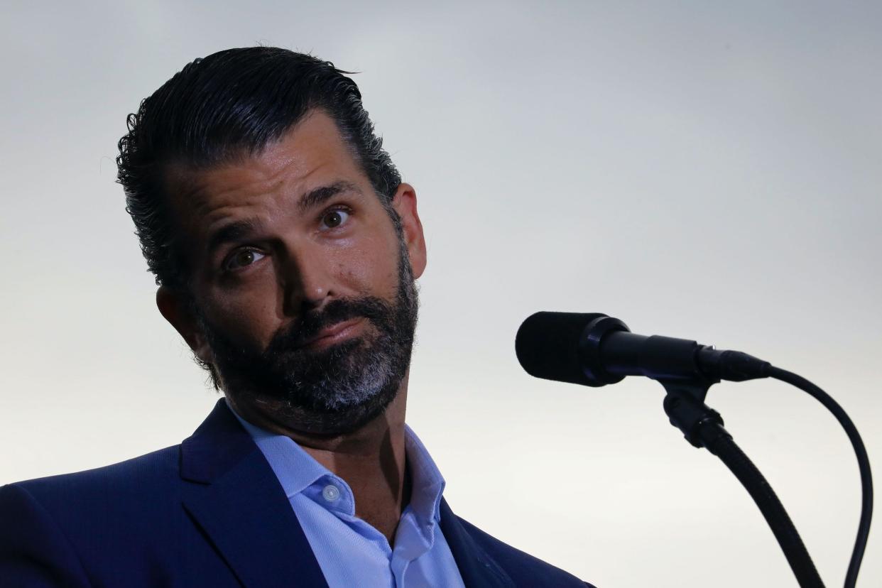 Donald Trump Jr. tilts his head and raises his eyebrows with his lips pursed behind the mic at a Trump rally.