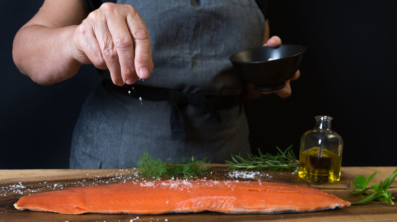 A chef salts a salmon filet