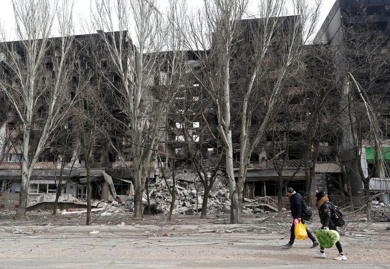 Local residents walk past a destroyed apartment building in Mariupol.