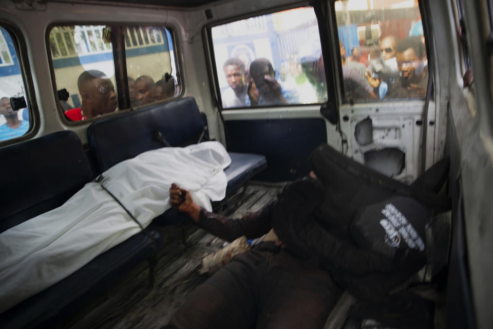 FILE - In this July 8, 2021 file photo, residents look into a police car window at the bodies of two unidentified people who Haitian Police Chief Leon Charles called suspects in the assassination of Haitian President Jovenel Moïse, following a shooting with police in Port-au-Prince, Haiti. Haitian authorities have implicated at least 20 retired Colombian soldiers in the president's assassination on July 7, and at least three of the Colombians were killed. (AP Photo/Joseph Odelyn, File)