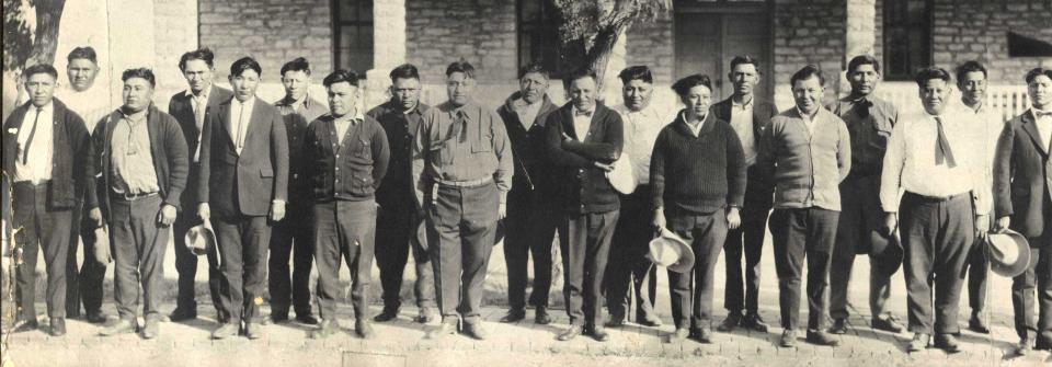 Comanche Nation citizens gather in front of Fort Sill Indian school before their induction into the Army during World War I. They are, from l-r, Dewy Maddox, Thompson Wermy Pekah, Casey Tomah, Samuel Pewewardy Sr., Guy Powetowaup, John Pahdopony, Jacob Wahkinney, James Wermy Pekah, John Wahkahquah, John Saupitty, Samuel Tahmahkera, Herbert Homovich, Samuel Tabbytosavit, Edward Clark, Bert Cable, Royce Tiddark, Edward Albert Nahquaddy Sr., Calvin Atchavit, Mikey Tahdooahnippah, William Tarcypokeahdooah, Abner Coosewoon, Jerry Saupitty and James Tahkofper. Although the exact date of the photograph is unknown, it had to have been taken sometime before March 1918.