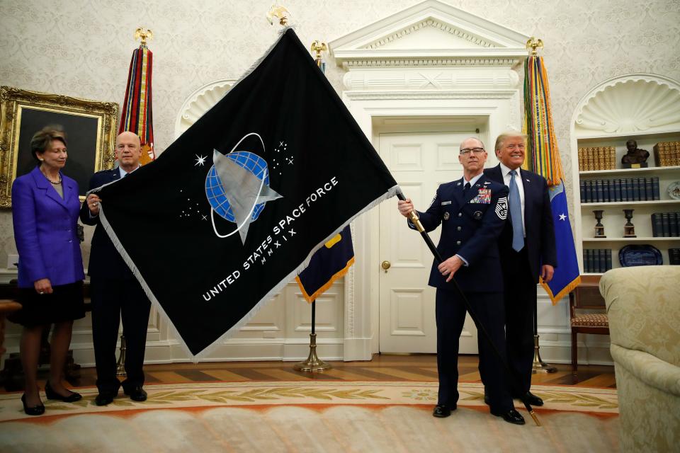 President Donald Trump stands as Chief of Space Operations at US Space Force Gen. John Raymond, second from left, and Chief Master Sgt. Roger Towberman, second from right, hold the United States Space Force flag as it is presented in the Oval Office of the White House, Friday, May 15, 2020, in Washington.  Secretary of the Air Force Barbara Barrett stands far left. (AP Photo/Alex Brandon) ORG XMIT: DCAB455