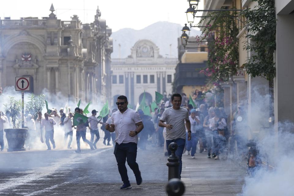 People run for cover as police launch tear gas to disperse demonstrators trying to reach Government Palace to demand the resignation of President Dina Boluarte, in Lima, Peru, Friday, April 5, 2024. Boluarte testified to prosecutors behind closed doors Friday as authorities investigate whether she illegally received hundreds of thousands of dollars in cash, luxury watches and jewelry. (AP Photo/Martin Mejia)