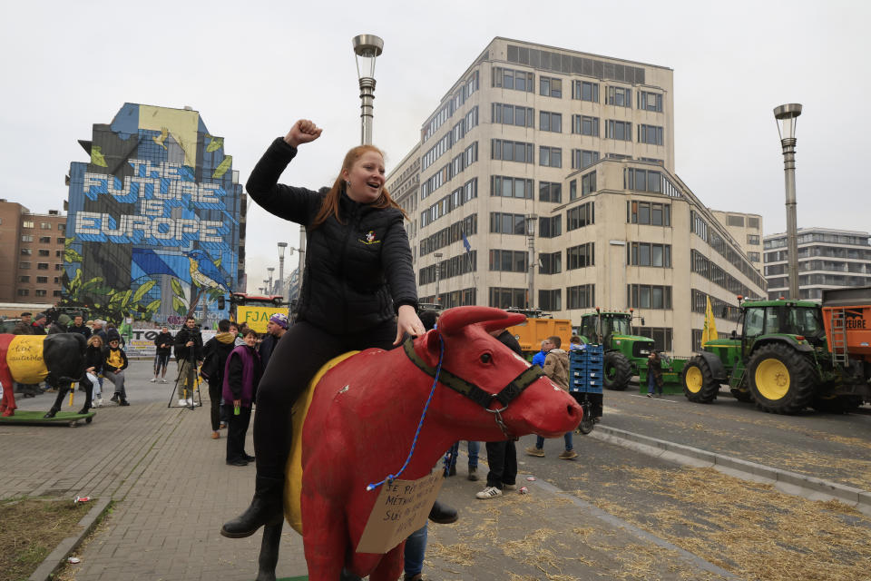 A protestor rides a plastic cow during a demonstration of farmers near the European Council building in Brussels, Tuesday, March 26, 2024. Dozens of tractors sealed off streets close to European Union headquarters where the 27 EU farm ministers are meeting to discuss the crisis in the sector which has led to months of demonstrations across the bloc. (AP Photo/Geert Vanden Wijngaert)