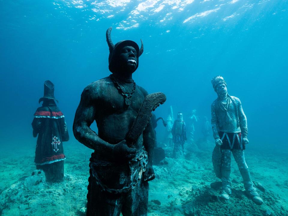 An underwater sculpture of the Jab Jab Spicemas masquerader, who wears a hat with horns and chains.