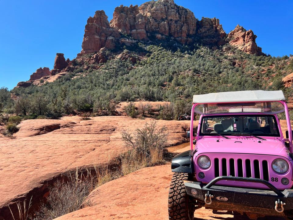 A pink jeep parked in front of red rock formations in Sedona.