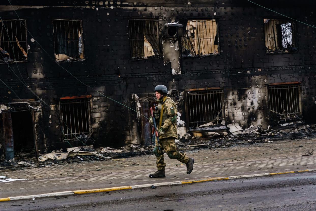 A Ukrainian soldier walks past a war-ravaged building.