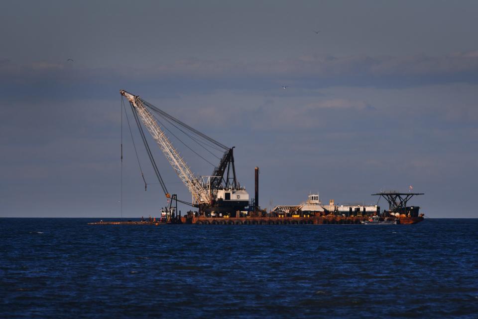A crane and barge can be seen working near West Gate Cocoa Beach Pier, trying to recover a barge from the ocean.