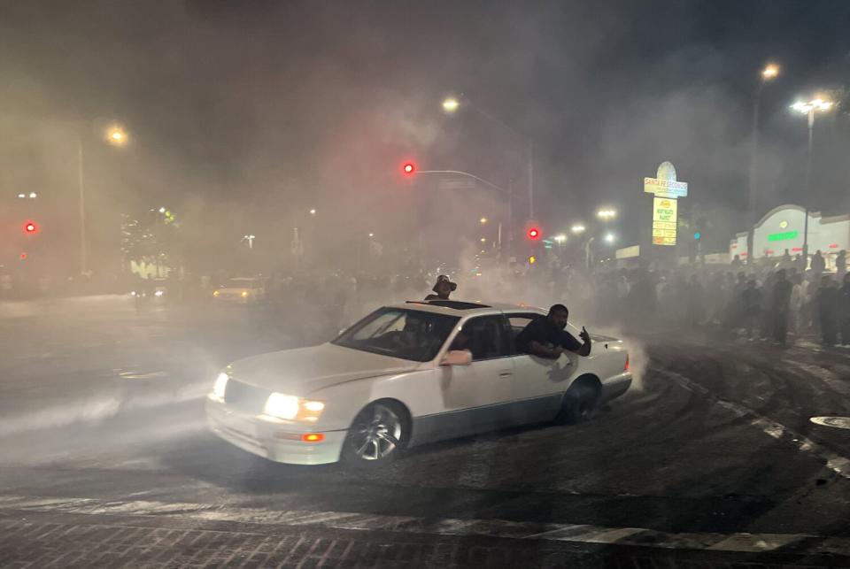 Passengers hang out of a spinning car at an early morning street takeover