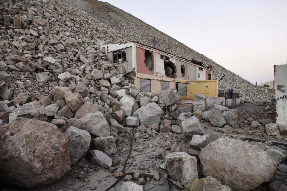 In this Sept. 25, 2012 photo, an structure with huge holes in its roof and walls, caused by falling rocks, sits abandoned in an area that used to be a town where miners lived at the Chuquicamata copper mine in the Atacama desert in northern Chile. The town was moved as the mine grew. Experts say that by 2019 the Chuquicamata copper mine will be unprofitable, so state-owned mining company Codelco is trying to head off closure by converting the open pit into the world's largest underground mine. Codelco believes the mine still has much more to give, with reserves equal to about 60 percent of all the copper exploited in the mine's history still buried deep beneath the crater. (AP Photo/Jorge Saenz)