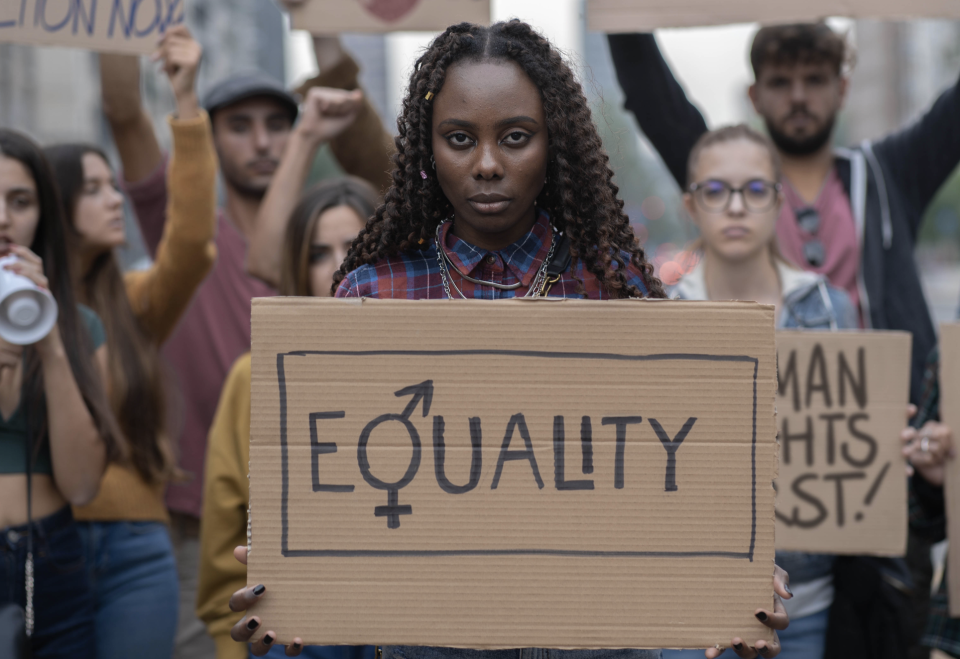 Woman holding up a sign that says "Equality" at a protest with other protestors behind her