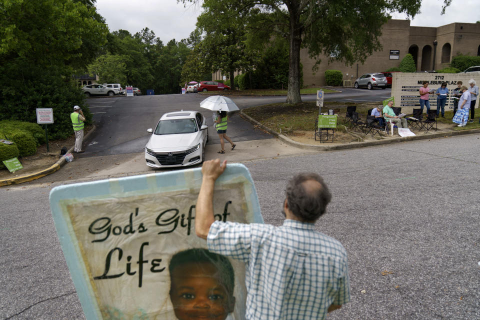 Anti-abortion protester Steven Lefemine, holds a sign as the anti-abortion group, A Moment of Hope, wearing green vests, tries to talk with patients arriving for abortion appointments at Planned Parenthood next to a group of Catholics praying off to the side, Friday, May 27, 2022, in Columbia, S.C. Mark Baumgartner, founder of A Moment of Hope wishes Lefemine didn't bring his big foam signs. "They're expecting to get yelled at that they're going to hell," says Baumgartner, who left behind his job as a pilot to create the organization. "We're here to be different." (AP Photo/David Goldman)