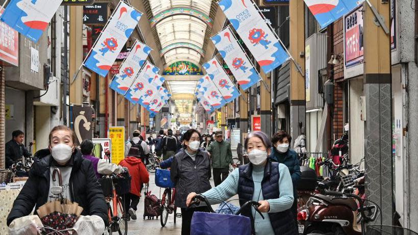 Women wearing masks riding their bicycles on a street in Japan. 