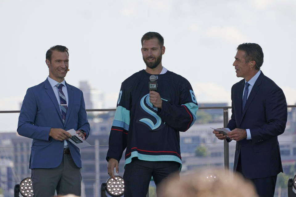 Chris Dreidger, center, a goalie from the Florida Panthers, stands with ESPN NHL hockey draft hosts Dominic Moore, left, and Chris Fowler as he is introduced Wednesday, July 21, 2021, as a new player for the Seattle Kraken during the team's expansion draft event in Seattle. (AP Photo/Ted S. Warren)