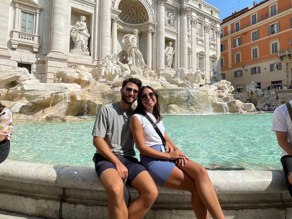 Victoria Craparotta and Flavio Fabiani sitting at the edge of the Trevi Fountain in Rome.