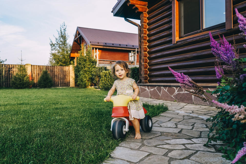 A little girl is riding a toy bike in a backyard