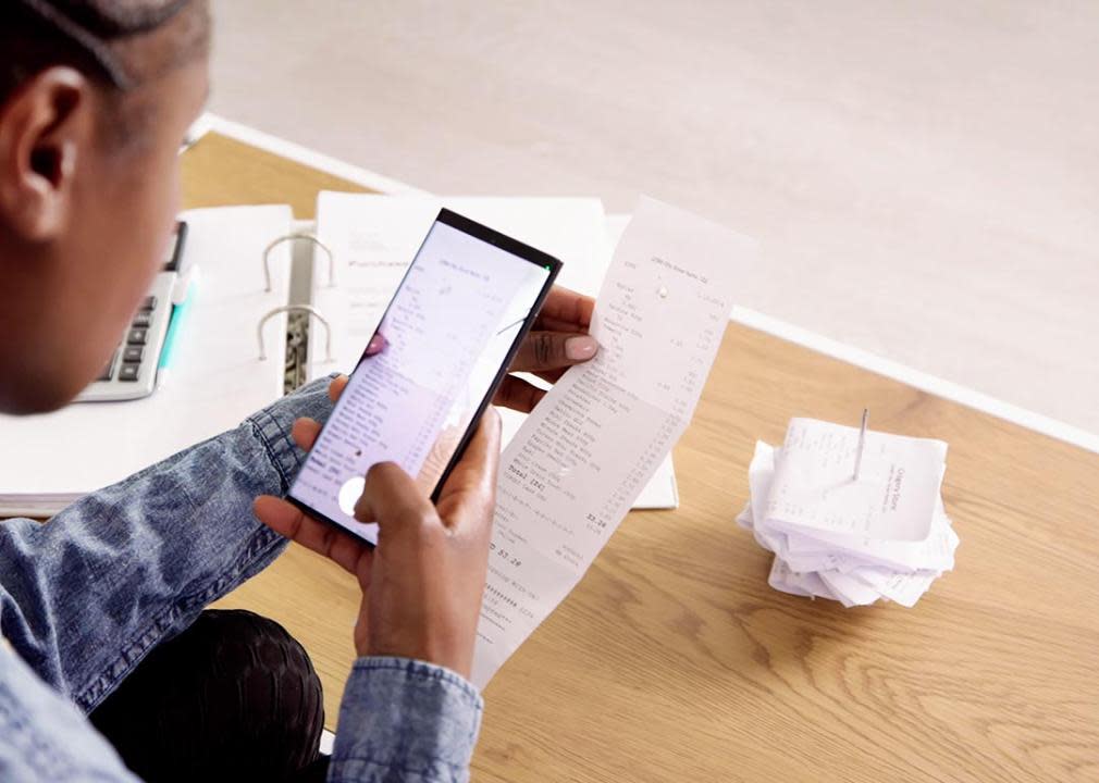 Person sitting at coffee table checking financial information on phone.